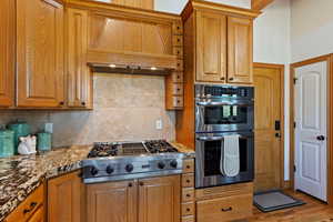 Kitchen with light hardwood / wood-style flooring, stainless steel appliances, premium range hood, and backsplash