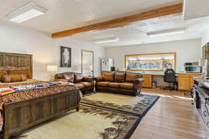 Very large Bedroom #5 with built in desk, light hardwood / wood-style floors, a textured ceiling, and beam ceiling