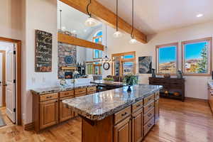 Kitchen with a kitchen island, light wood-type flooring, stone countertops, a stone fireplace, and decorative light fixtures