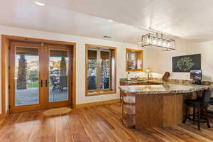 Kitchenette with wet bar with french doors, a textured ceiling, kitchen peninsula, pendant lighting, and light hardwood / wood-style flooring