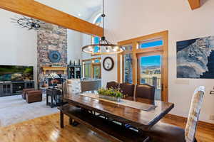 Dining space with ceiling fan with notable chandelier, hardwood / wood-style flooring, high vaulted ceiling, and a fireplace