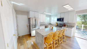 Kitchen with a healthy amount of sunlight, a kitchen island, a kitchen breakfast bar, stainless steel appliances, and light hardwood / wood-style flooring