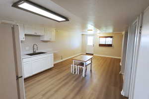 Kitchen with sink, light wood-type flooring, a textured ceiling, white cabinetry, and white refrigerator