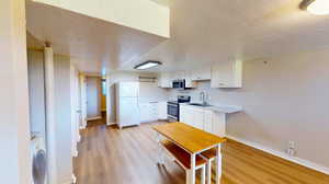 Kitchen featuring sink, light wood-type flooring, a textured ceiling, white cabinetry, and stainless steel appliances