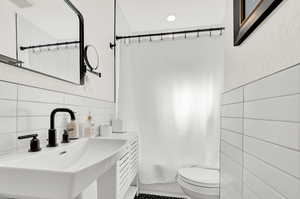 Full bathroom featuring sink, shower / bath combination with curtain, toilet, tile walls, and decorative backsplash