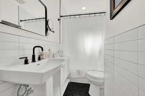 Full bathroom with decorative backsplash, shower / tub combo, tile walls, toilet, and sink