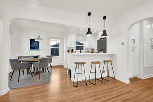 Kitchen with kitchen peninsula, white cabinetry, stainless steel refrigerator, light hardwood / wood-style flooring, and pendant lighting