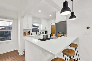 Kitchen featuring decorative backsplash, kitchen peninsula, wood-type flooring, sink, and white cabinetry