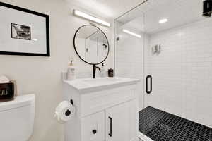 Bathroom with toilet, a shower with shower door, and vanity