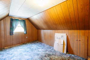 Additional living space featuring vaulted ceiling, carpet floors, and wooden walls