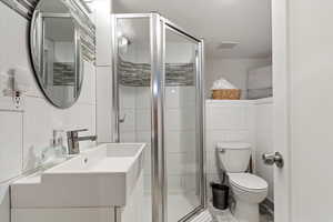 Bathroom with vanity, toilet, walk in shower, and tile walls