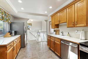 Kitchen with light tile patterned floors, appliances with stainless steel finishes, a raised ceiling, ornamental molding, and sink