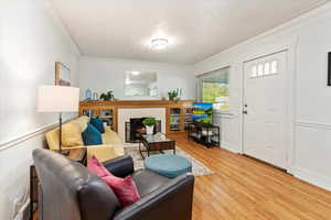 Living room featuring crown molding, a textured ceiling, a tiled fireplace, and light wood-type flooring