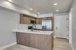 Kitchen featuring appliances with stainless steel finishes, kitchen peninsula, light hardwood / wood-style flooring, and sink