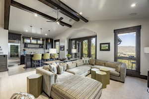 Living room with vaulted ceiling with beams, ceiling fan, light colored carpet, and a wealth of natural light