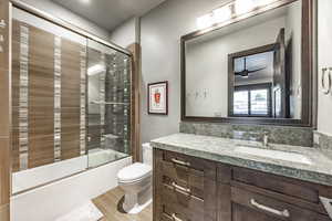 Full bathroom featuring bath / shower combo with glass door, vanity, ceiling fan, wood-type flooring, and toilet