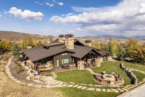 Rear view of property featuring a mountain view, a yard, a patio, and an outdoor living space with a fire pit