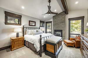 Carpeted bedroom featuring a fireplace, vaulted ceiling with beams, and ceiling fan