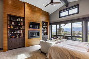 Bedroom featuring ceiling fan, wooden walls, beam ceiling, high vaulted ceiling, and a fireplace