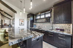 Kitchen featuring light stone countertops, hanging light fixtures, vaulted ceiling with beams, a kitchen bar, and decorative backsplash