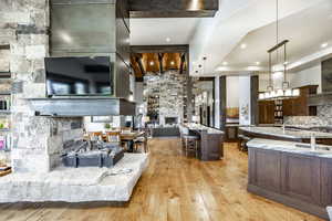 Kitchen with light stone countertops, a stone fireplace, light hardwood / wood-style flooring, a large island with sink, and pendant lighting