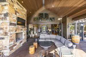 Living room featuring an outdoor stone fireplace, high vaulted ceiling, plenty of natural light, and wood ceiling