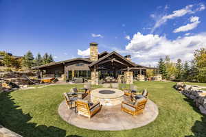 Back of house featuring ceiling fan, a patio, an outdoor fire pit, and a lawn