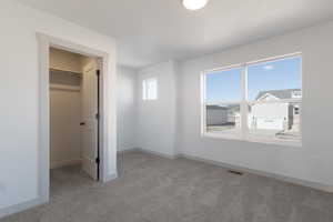 Unfurnished bedroom with a spacious closet, light colored carpet, and a closet