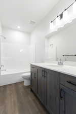 Full bathroom featuring toilet, vanity, wood-type flooring, and washtub / shower combination