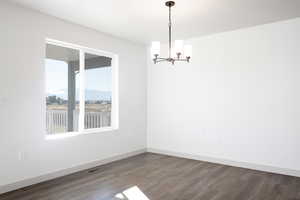 Empty room with a notable chandelier and dark hardwood / wood-style flooring