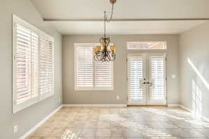 Unfurnished dining area featuring french doors, light tile patterned flooring, an inviting chandelier, and plenty of natural light