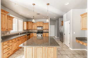 Kitchen with decorative backsplash, appliances with stainless steel finishes, dark stone counters, and a kitchen island