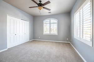 Unfurnished bedroom with a closet, ceiling fan, multiple windows, and carpet floors