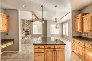 Kitchen with decorative backsplash, light hardwood / wood-style flooring, a stone fireplace, lofted ceiling with beams, and decorative light fixtures