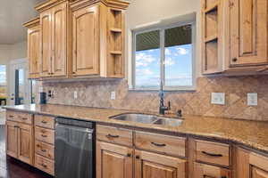 Kitchen with decorative backsplash, sink, stainless steel dishwasher, light stone counters, and dark hardwood / wood-style flooring