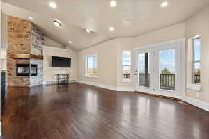 Unfurnished living room with a stone fireplace, high vaulted ceiling, and dark wood-type flooring