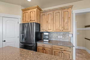 Kitchen featuring stone countertops, backsplash, tile patterned floors, light brown cabinets, and stainless steel refrigerator with ice dispenser