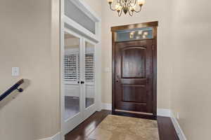 Foyer featuring dark wood-type flooring, a notable chandelier, and french doors