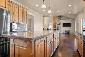 Kitchen with lofted ceiling, a kitchen island, backsplash, stainless steel fridge, and dark hardwood / wood-style flooring