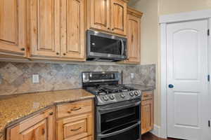 Kitchen featuring light stone countertops, decorative backsplash, appliances with stainless steel finishes, and dark hardwood / wood-style floors