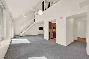 Unfurnished living room featuring light carpet, high vaulted ceiling, and sink