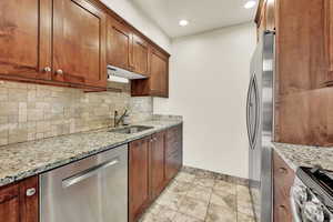 Kitchen with light stone countertops, sink, appliances with stainless steel finishes, and backsplash