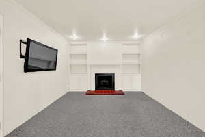 Unfurnished living room with crown molding, carpet flooring, a fireplace, and built in shelves