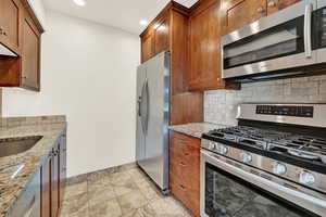 Kitchen featuring stainless steel appliances, light stone countertops, sink, and tasteful backsplash