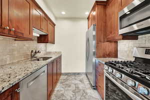 Kitchen featuring appliances with stainless steel finishes, light stone countertops, sink, and backsplash