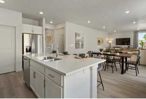 Kitchen with stainless steel appliances, a center island with sink, sink, light wood-type flooring, and white cabinets