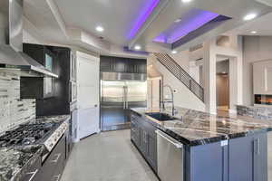 Kitchen with wall chimney exhaust hood, sink, appliances with stainless steel finishes, and backsplash