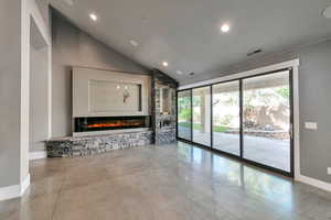 Unfurnished living room with lofted ceiling, a stone fireplace, and concrete flooring