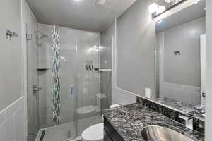 Bathroom with a textured ceiling, a shower with shower door, toilet, tile walls, and vanity