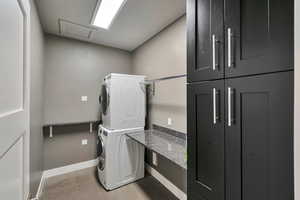 Laundry room with cabinets, light colored carpet, and stacked washer and clothes dryer